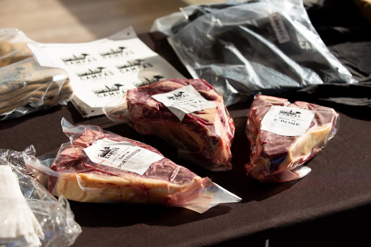 Kolme tyhjiöpakattua pihviä pöydällä: porterhouse, T-bone ja kolmas leike, jonka etiketti ei erotu selvästi. Etiketeissä lukee Campas Meats ja Finnish Black Angus. Taustalla Campas Meats -logotarroja sekä pinottuja pakkausmateriaaleja.