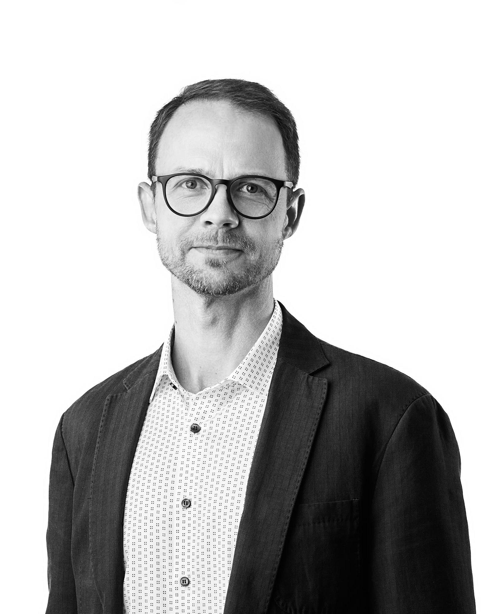 Mustavalkoinen henkilökuva Marko Hotokasta. Hänellä on pyöreät tummasankaiset silmälasit, lyhyet hiukset ja sänkiparta. Hän katsoo suoraan kameraan pienesti hymyillen. Yllään hänellä on tumma pikkutakki ja vaalea, pienikuvioinen kauluspaita. Taustana on valkoinen.